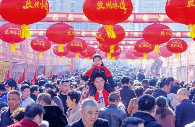 En pojke på sin pappas axlar äter tanghulu på en nyårsmarknad i Jiaozhou, Shandong-provinsen.