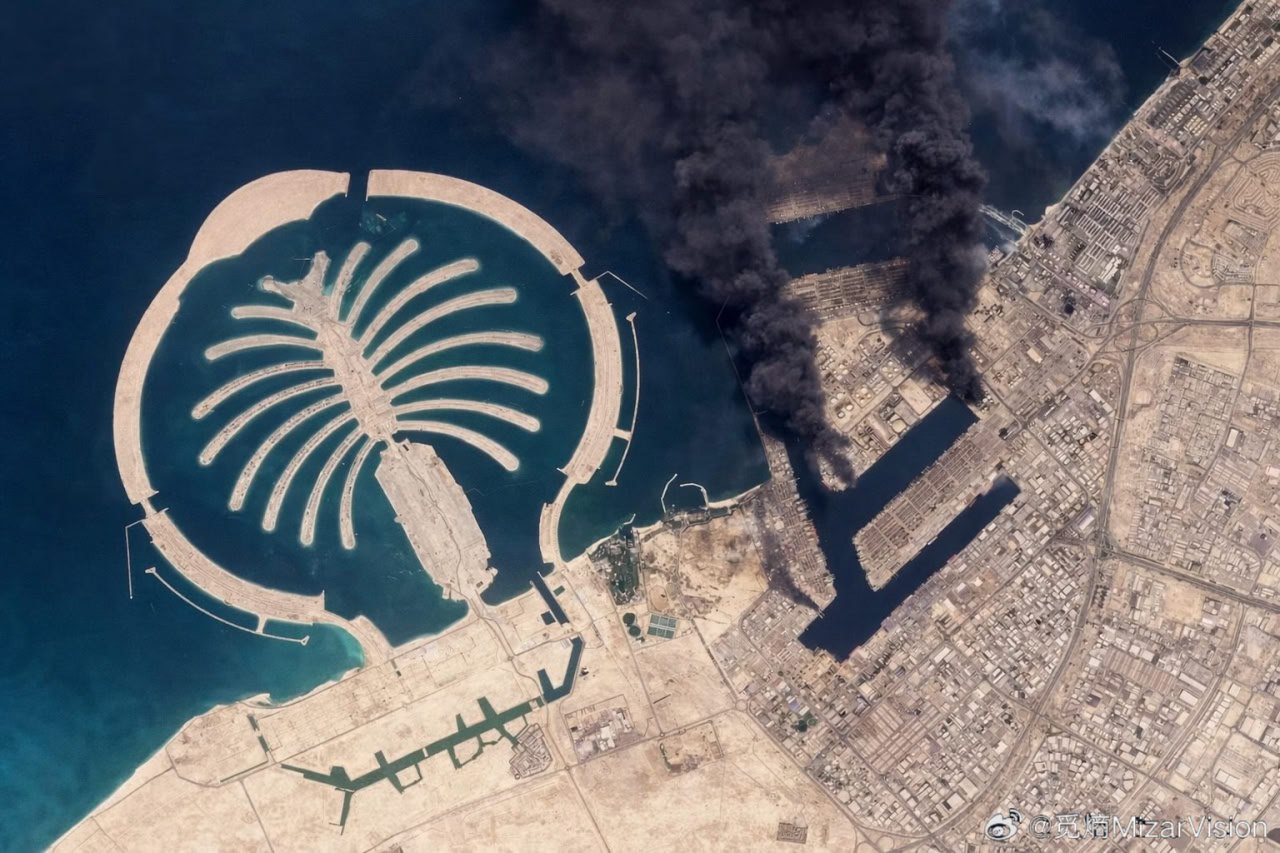 Satellitbild över Jebel Ali-hamnen i Dubai med massiva svarta rökpelare från brand i hamnområdet, Palm Jebel Ali syns till vänster