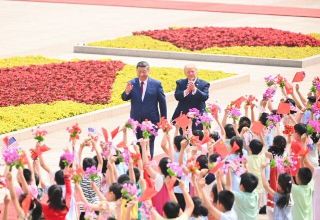 Xi Jinping vinkar och Donald Trump applåderar under en välkomstceremoni i Peking medan barn viftar med kinesiska och amerikanska flaggor.