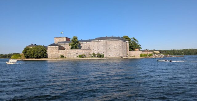 Vaxholms kastell med svensk flagga, sett från vattnet.