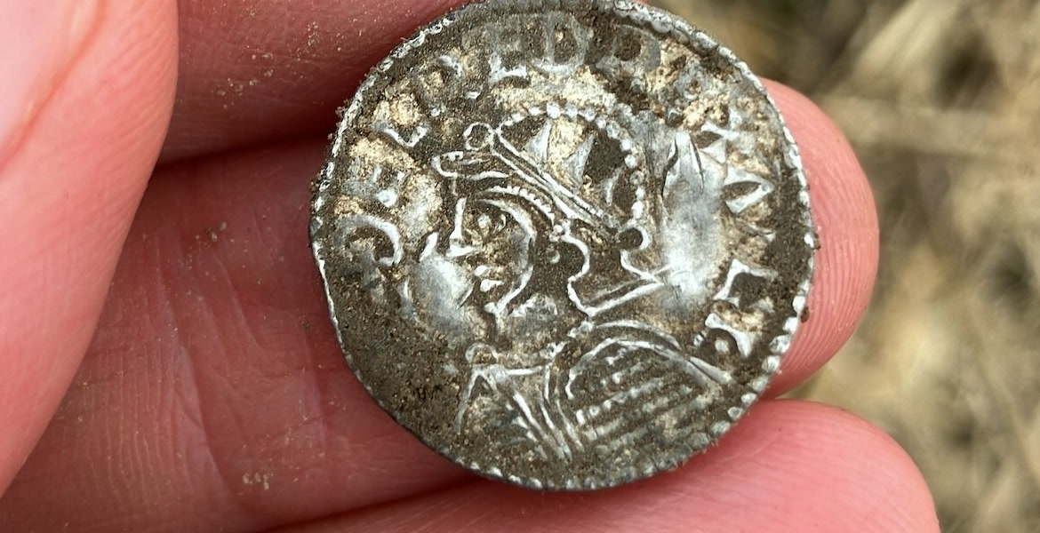 Vikingatida silvermynt med ett kungaporträtt hålls mellan fingrar