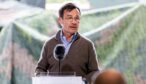 Ulf Kristersson talar vid en talarstol med mikrofon, i brun tröja och glasögon.