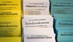 Gula, vita och blå partivalsedlar i ett valsedelställ, bland annat för Folkpartiet, Kristdemokraterna och Kommunistiska Partiet.