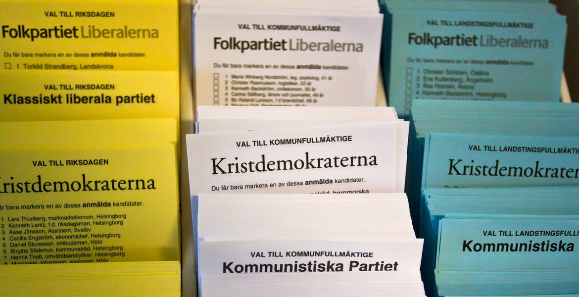 Gula, vita och blå partivalsedlar i ett valsedelställ, bland annat för Folkpartiet, Kristdemokraterna och Kommunistiska Partiet.