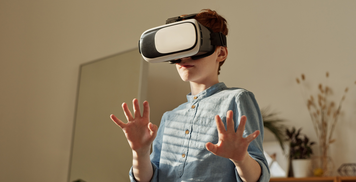 Genrebild av en pojke i blå skjorta med VR-headset och upplyfta händer i en inomhusmiljö.