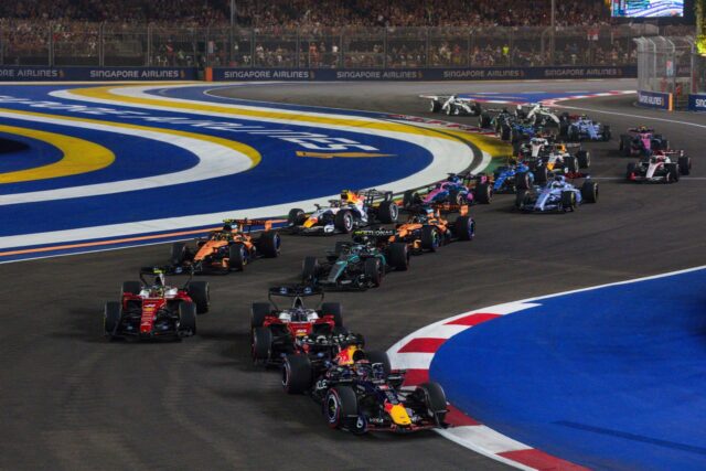 En Red Bull-bil framför två Ferrari-bilar och resten av Formel 1-fältet i en kurva på Marina Bay i Singapore.