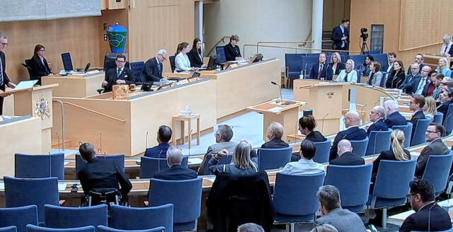 Riksdagens talarstol och presidium med ledamöter i förgrunden.